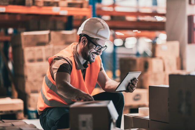 small-SINGLE-IMAGE_happy-white-male-warehouse-worker-with-boxes-checking-tablet-full-colour_july25